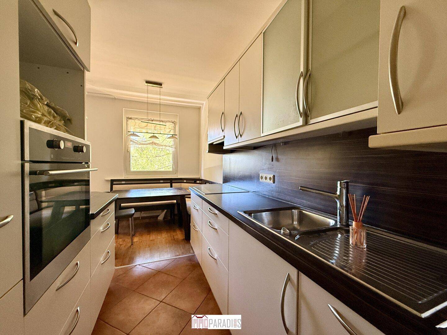 Gut ausgestattete Küche mit Backofen, Spüle und einem Essbereich im Hintergrund, ideal für den täglichen Gebrauch.