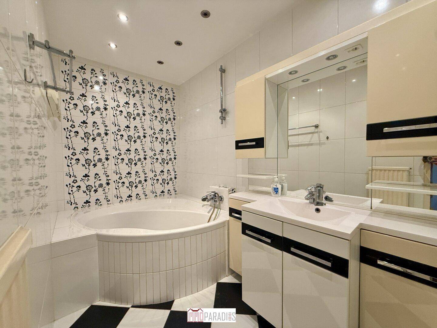 Badezimmer mit Eckbadewanne, Waschbecken und markanten schwarz-weißen Fliesen, die einen Kontrast bilden.