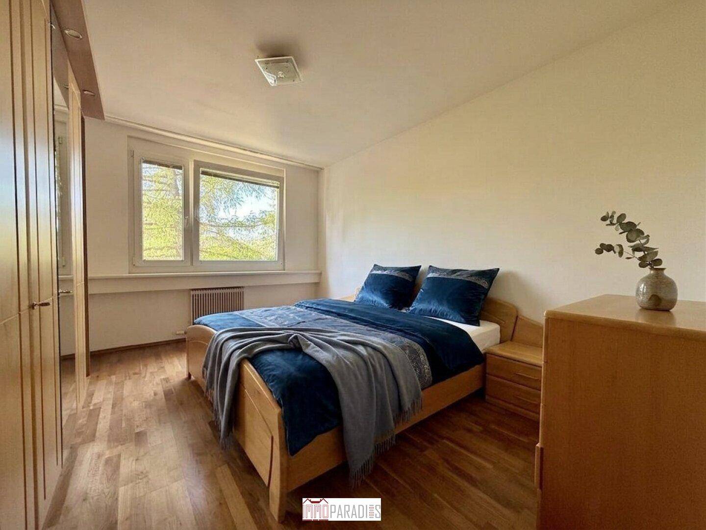 Gemütliches Schlafzimmer mit Holzboden, Doppelbett und Fenster, das eine ruhige Atmosphäre schafft.