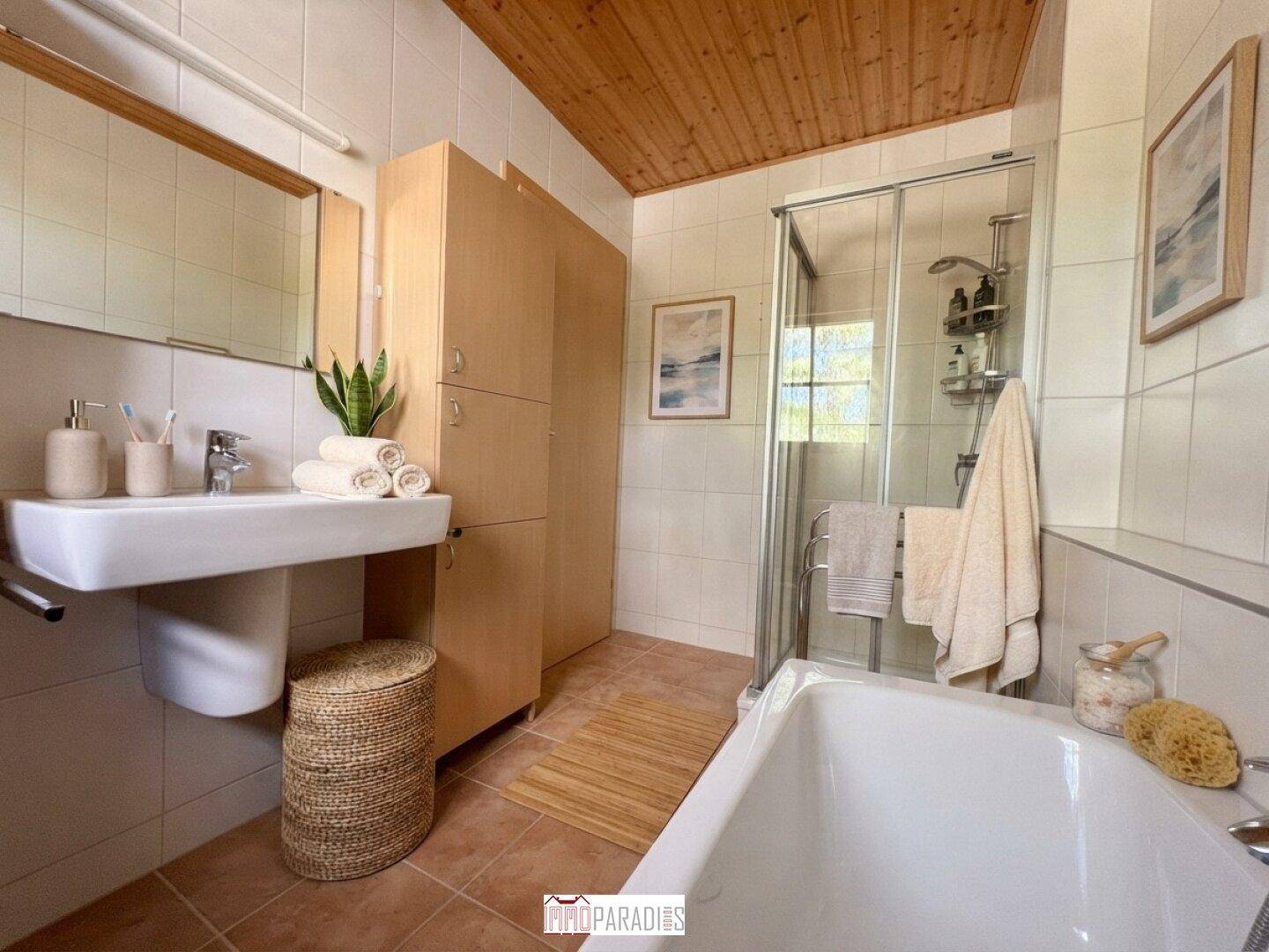 Badezimmer mit Badewanne, Dusche, Waschbecken und Holzdecke, hell gefliest.