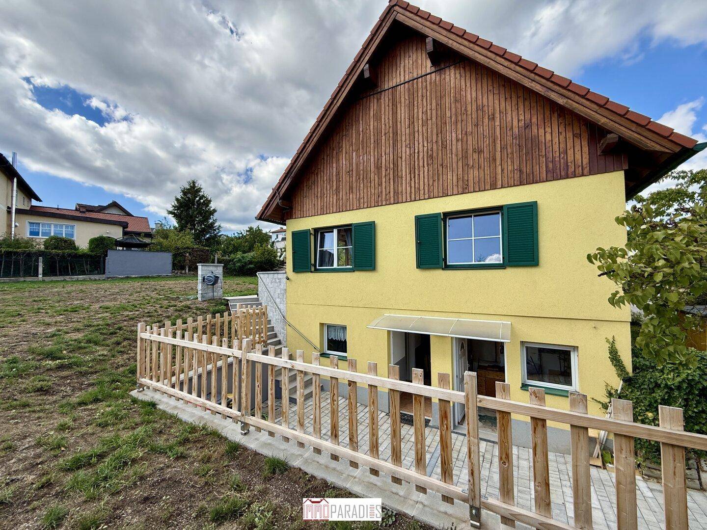 Rückansicht des Hauses mit gelber Fassade, Holzverkleidung und einem Gartenbereich.