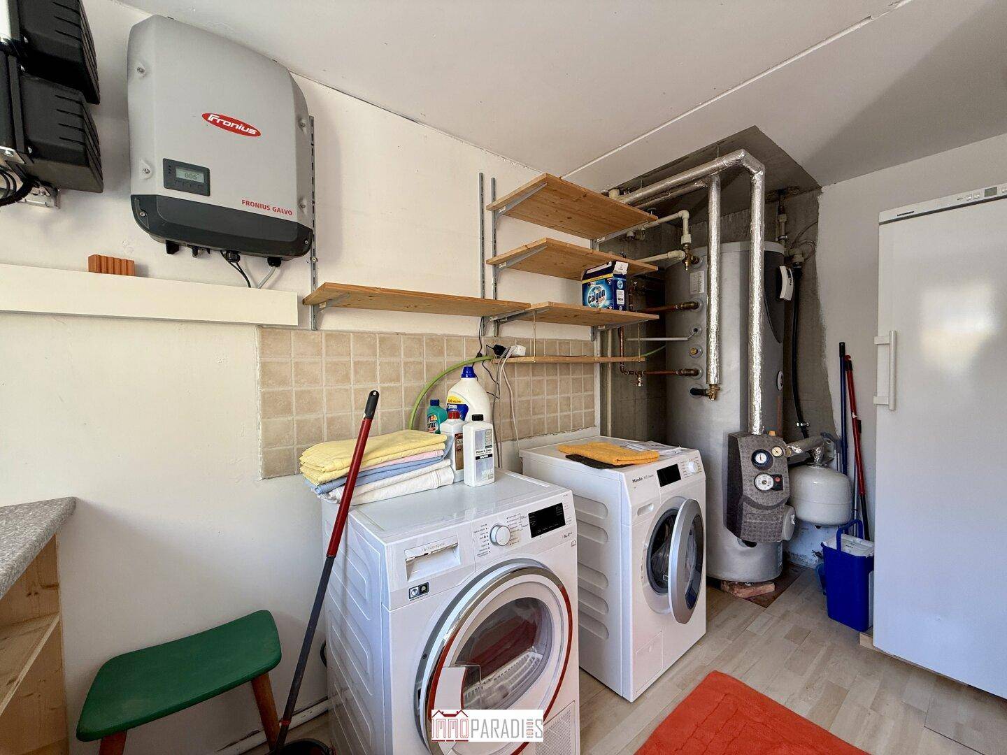Hauswirtschaftsraum mit Waschmaschine, Trockner, Heizungsanlage und Regalen für Stauraum.