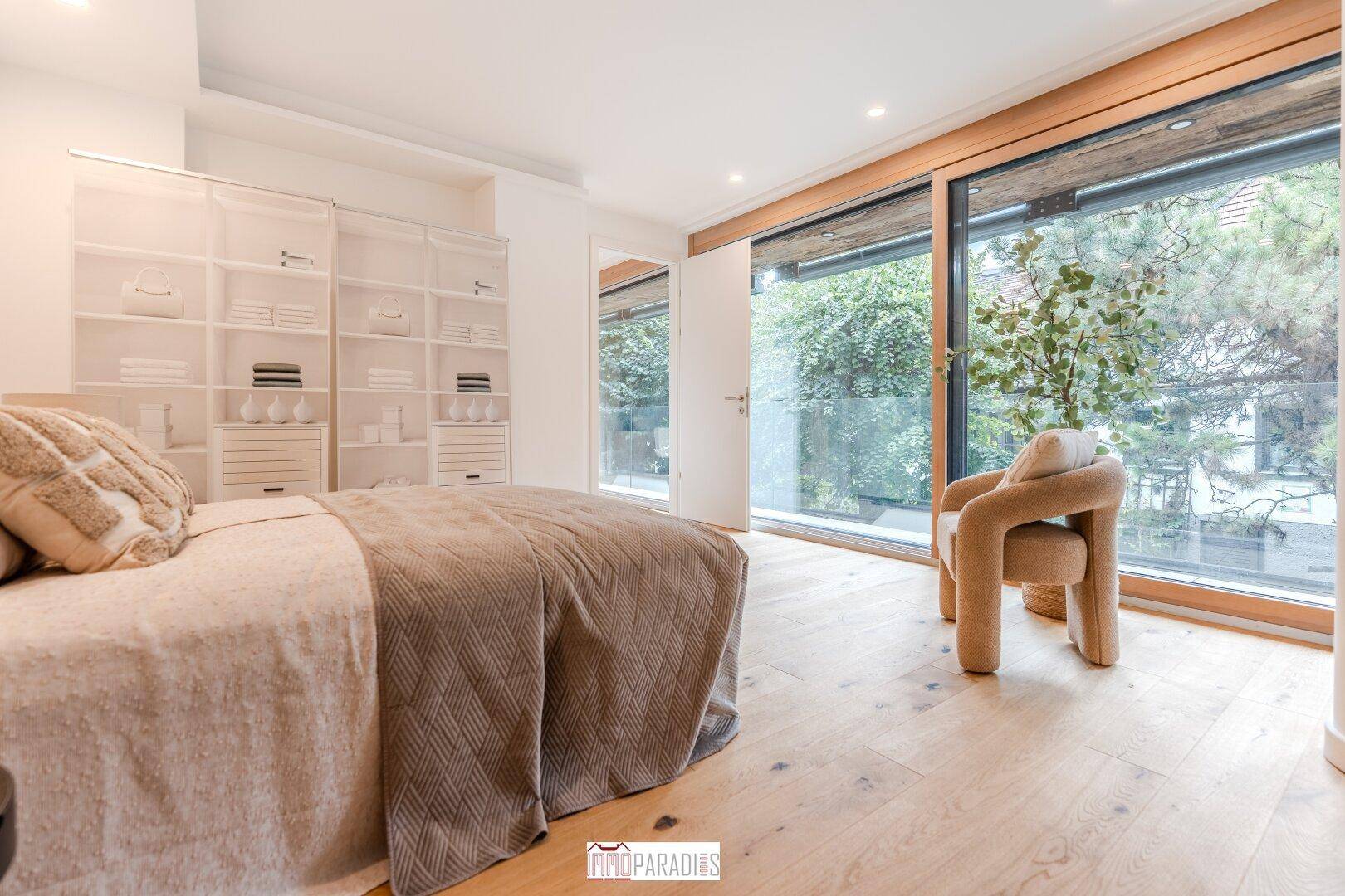 Helles Schlafzimmer mit Holzboden, großem Fenster und Blick ins Grüne.