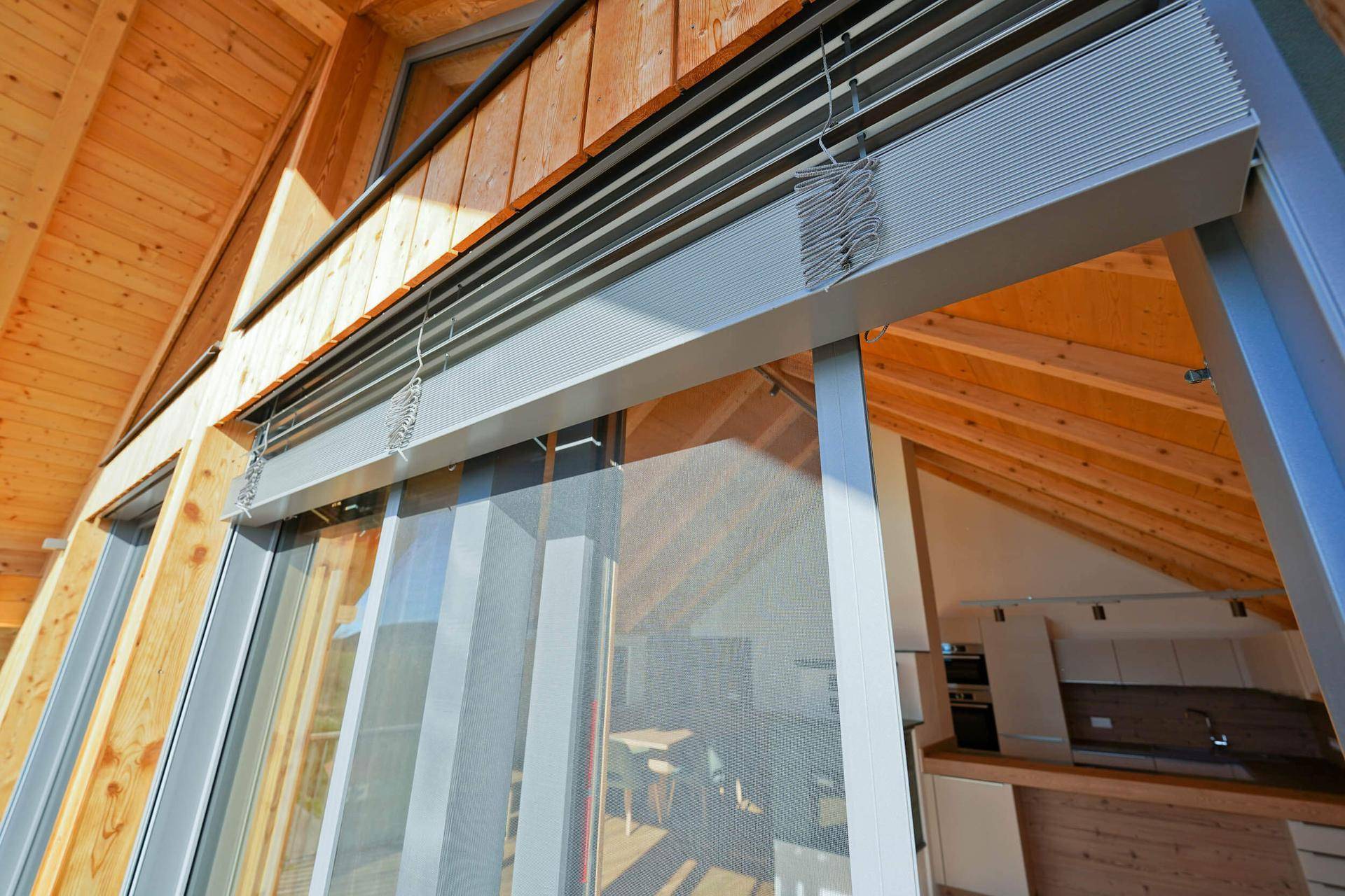 Große Fensterfront mit Jalousien und Holzdachschrägen, die viel natürliches Licht hereinlässt.