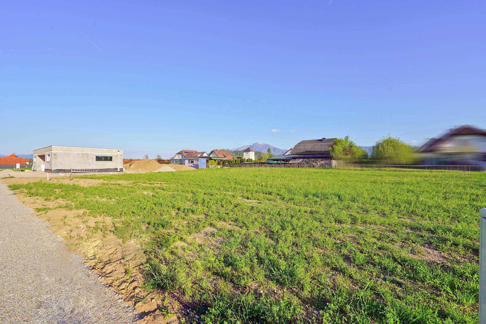 Baugrundstück mit teilweisem Neubau im Vordergrund und idyllischem Bergpanorama.