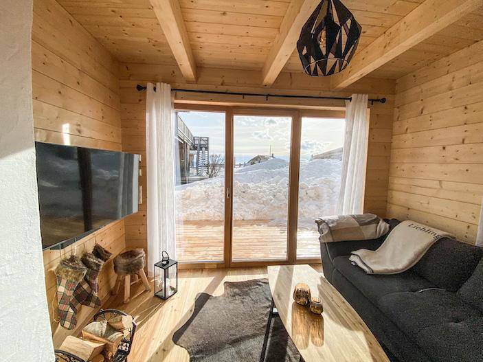 Helles Wohnzimmer mit großen Fenstern, Holzboden und Blick auf die verschneite Landschaft.