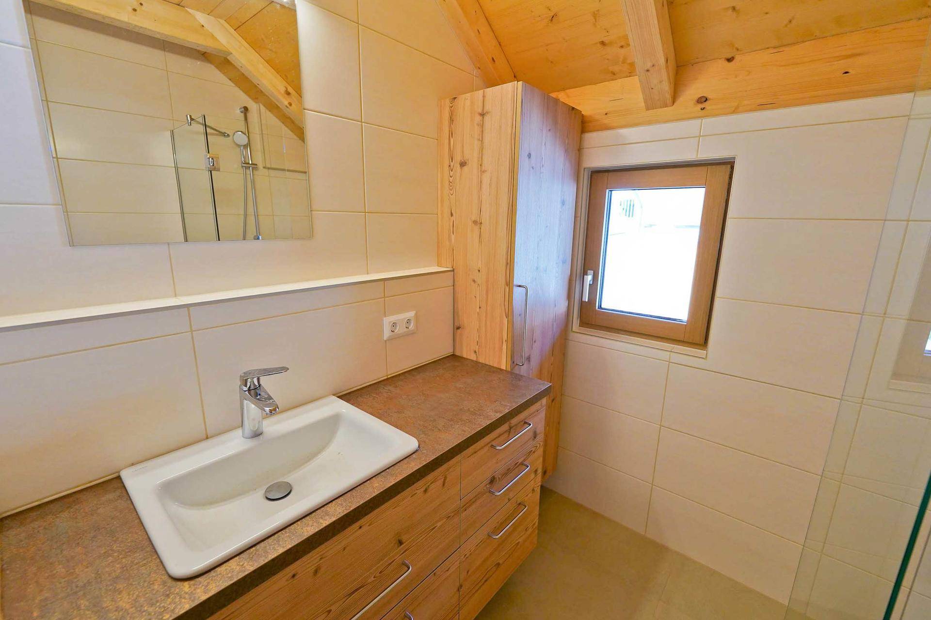 Helles Badezimmer mit Holzelementen, Einzelwaschbecken und Fenster unter der Dachschräge.