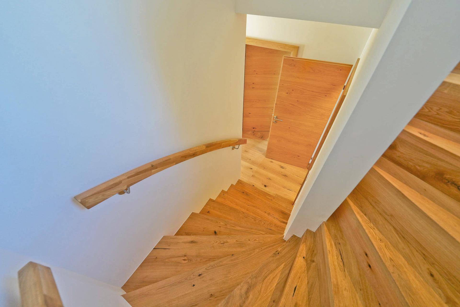 Geschwungene Holztreppe mit Handlauf verbindet die Etagen des Hauses in hellem Ambiente.