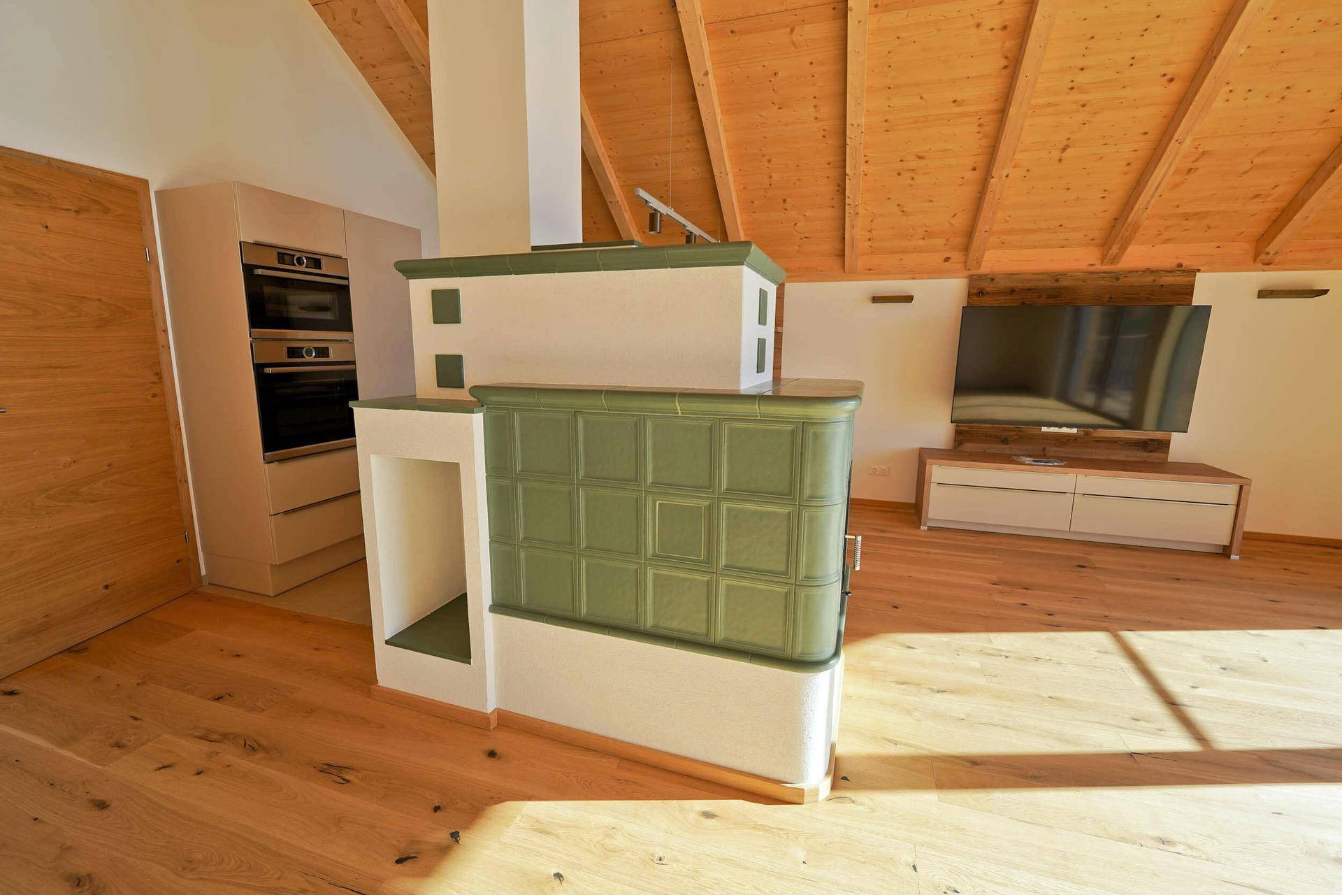 Gemütlicher Wohnbereich mit Kachelofen, Holzboden und Fernseher unter der Dachschräge.