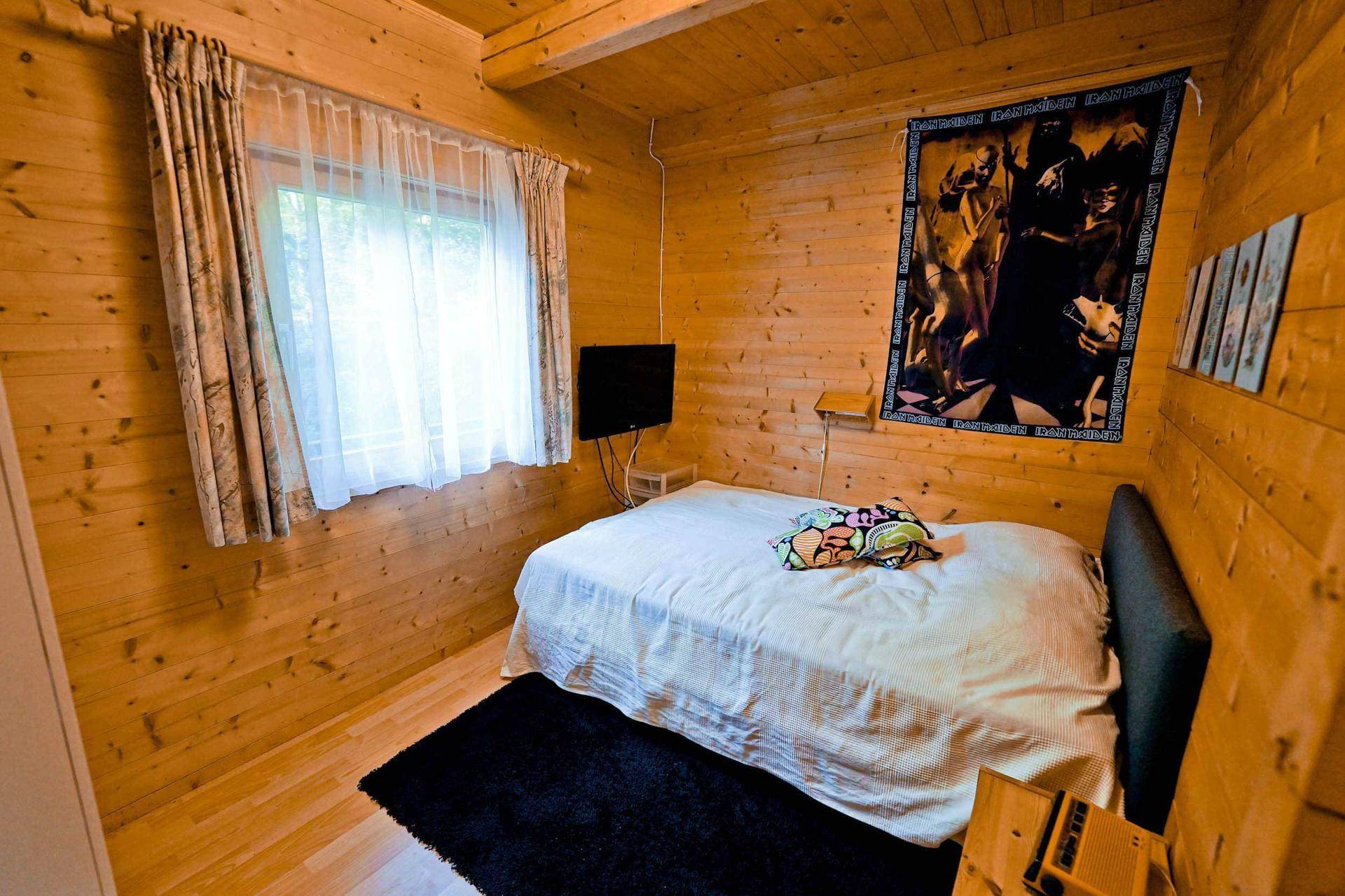 Kleines Schlafzimmer mit Holzwänden, Einzelbett und Fenster, das viel Tageslicht hereinlässt.