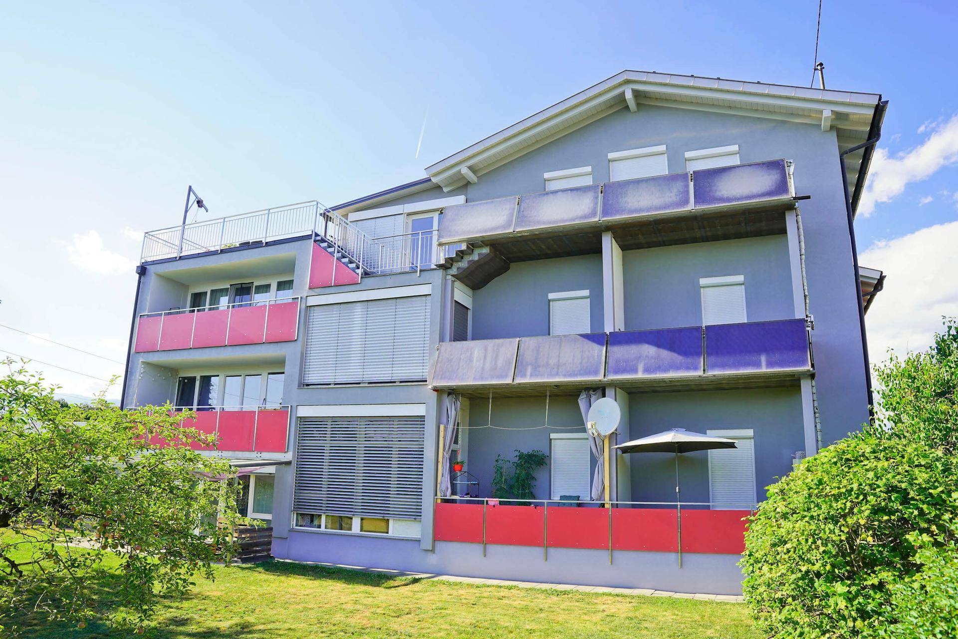 Moderne Wohnanlage mit mehreren Balkonen und einer Dachterrasse, umgeben von Grünflächen.