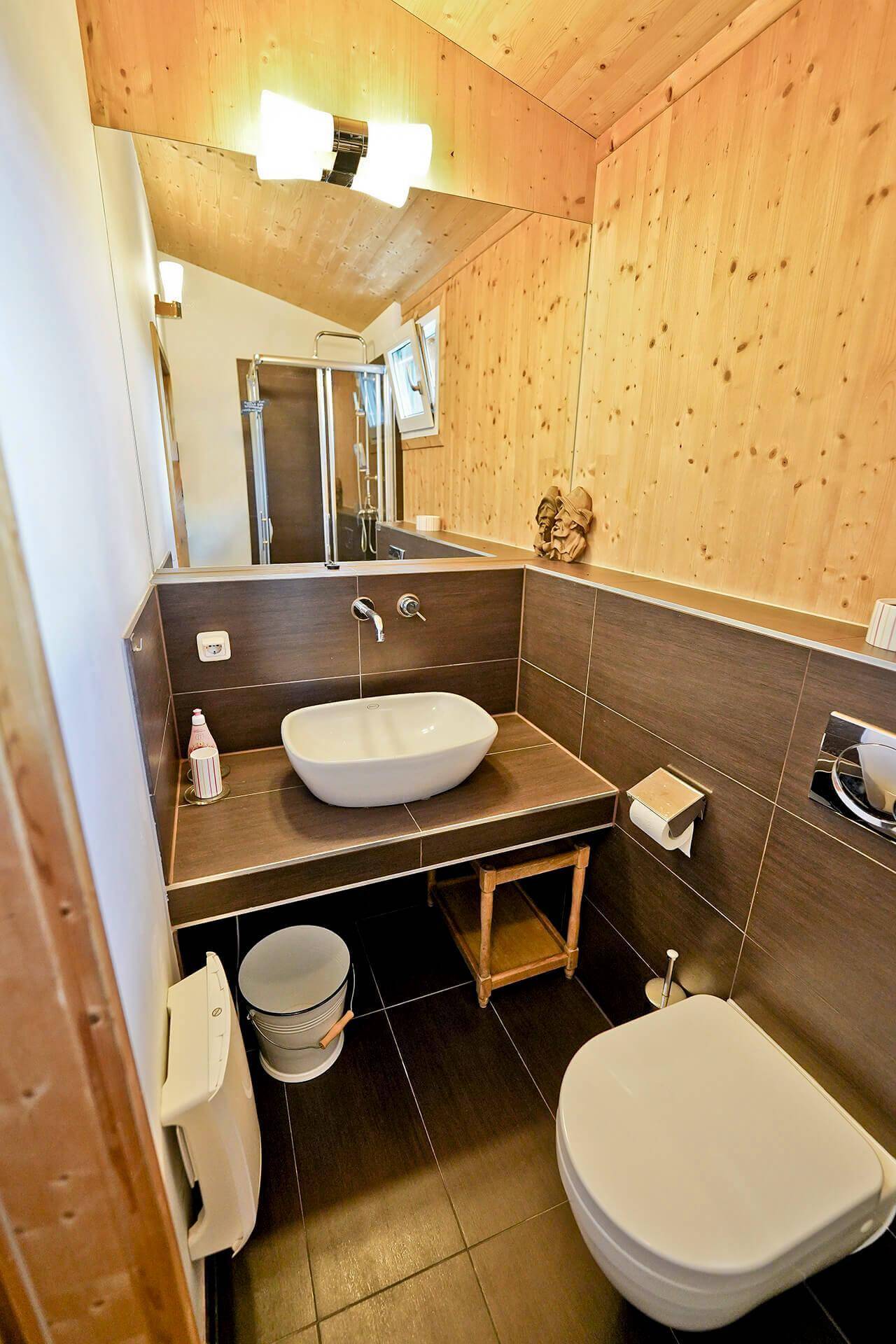 Modernes Badezimmer mit Holzwänden, Aufsatzwaschbecken, Toilette und großem Spiegel.