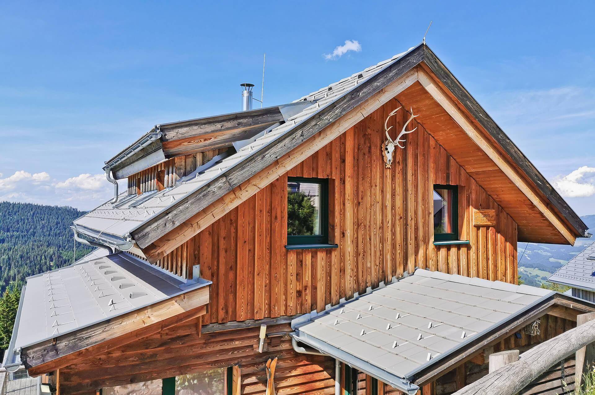 Seitenansicht des Holzchalets mit Satteldach und einem Hirschgeweih als traditionelle Dekoration.