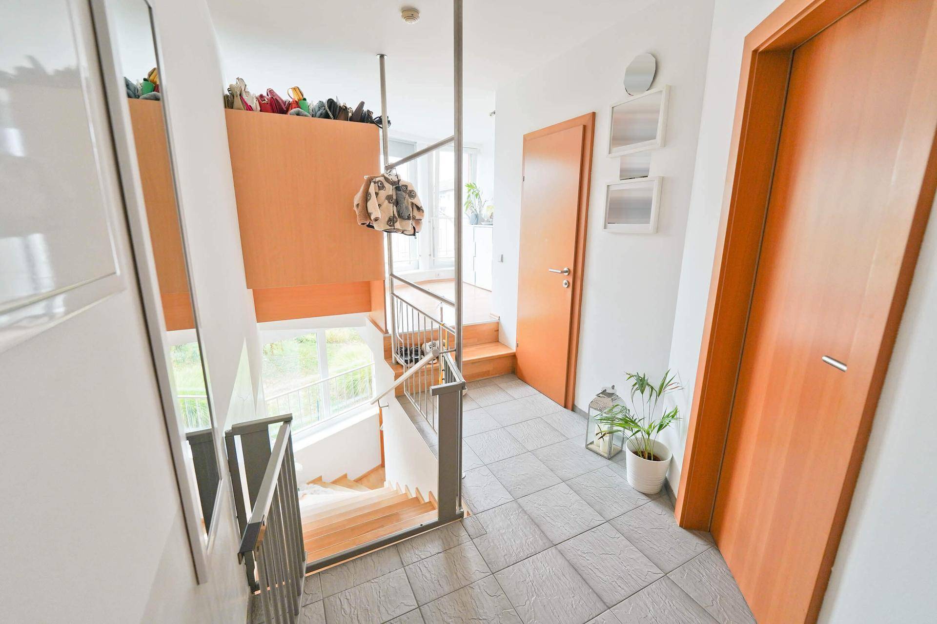 Heller Flur mit Treppenaufgang und -abgang, ausgestattet mit Fliesenboden und Holzdetails.