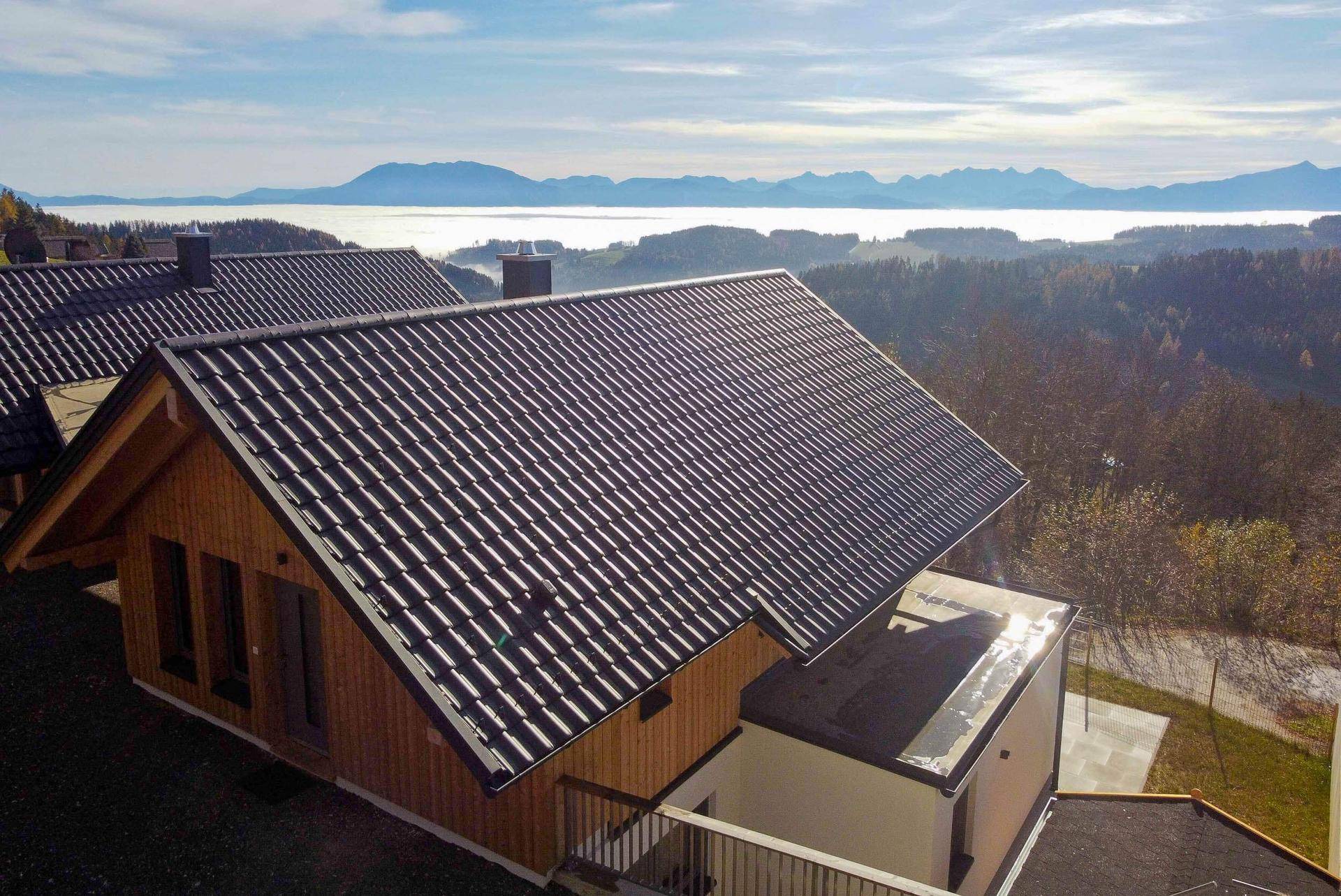 Dachansicht eines Holzhauses mit dunklem Ziegeldach und weitem Blick über die nebelverhangene Landschaft.