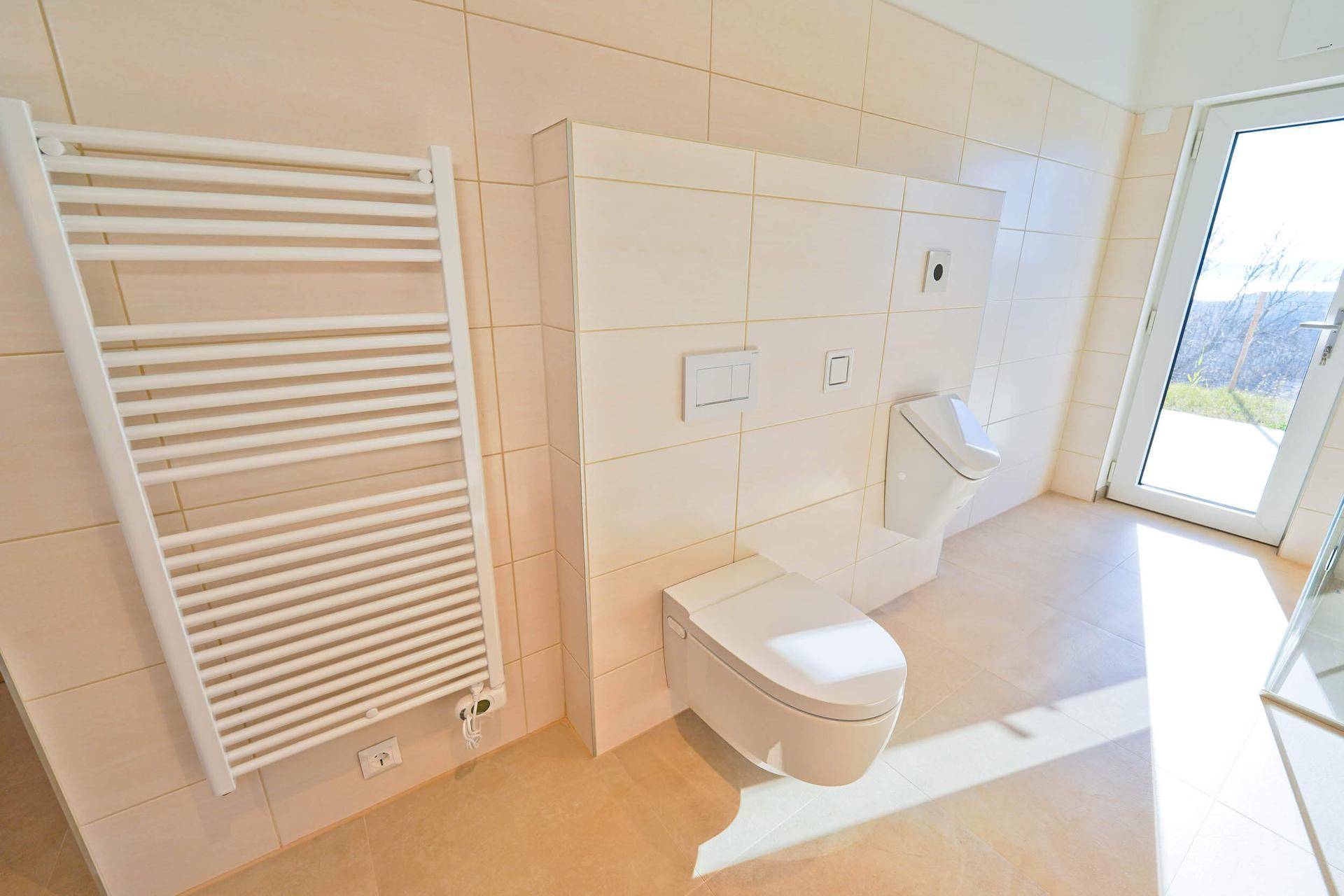Geräumiges Badezimmer mit Wand-WC, Urinal und beheiztem Handtuchhalter.