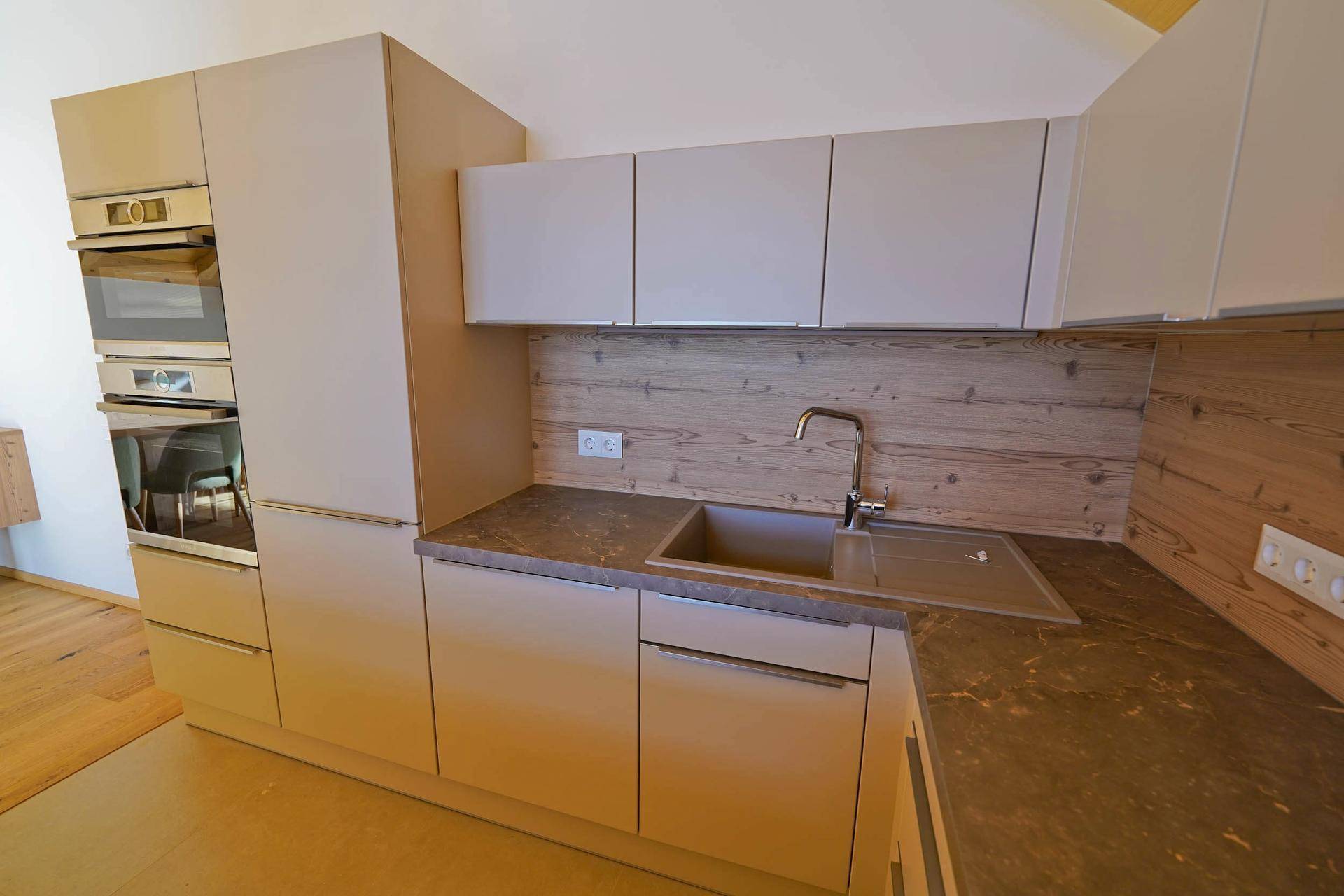 Funktionale Einbauküche mit Spüle, Backofen und Holzrückwand in hellem, modernem Design.