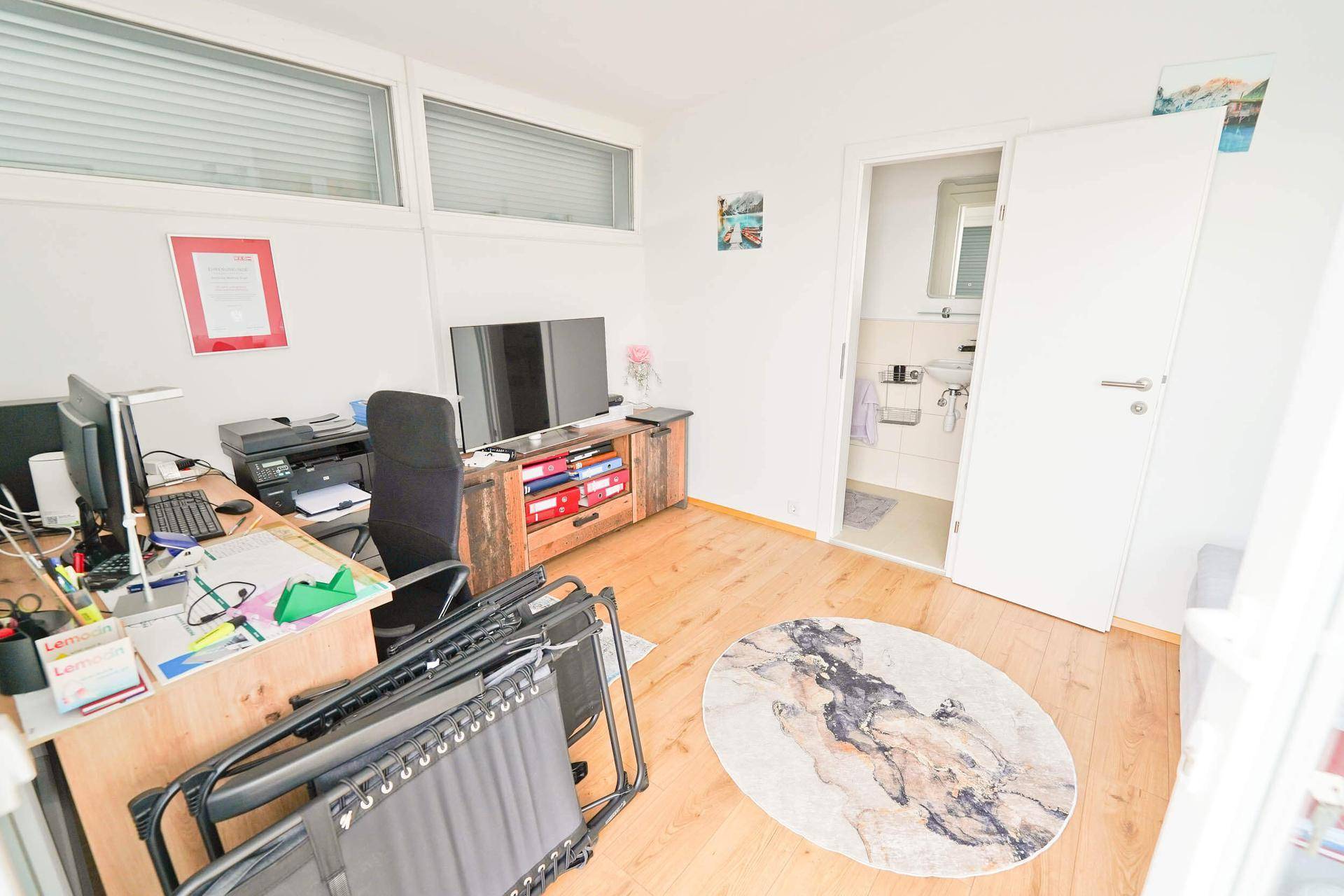 Helles Arbeitszimmer mit Holzboden, Schreibtisch und Zugang zu einem angrenzenden Badezimmer.