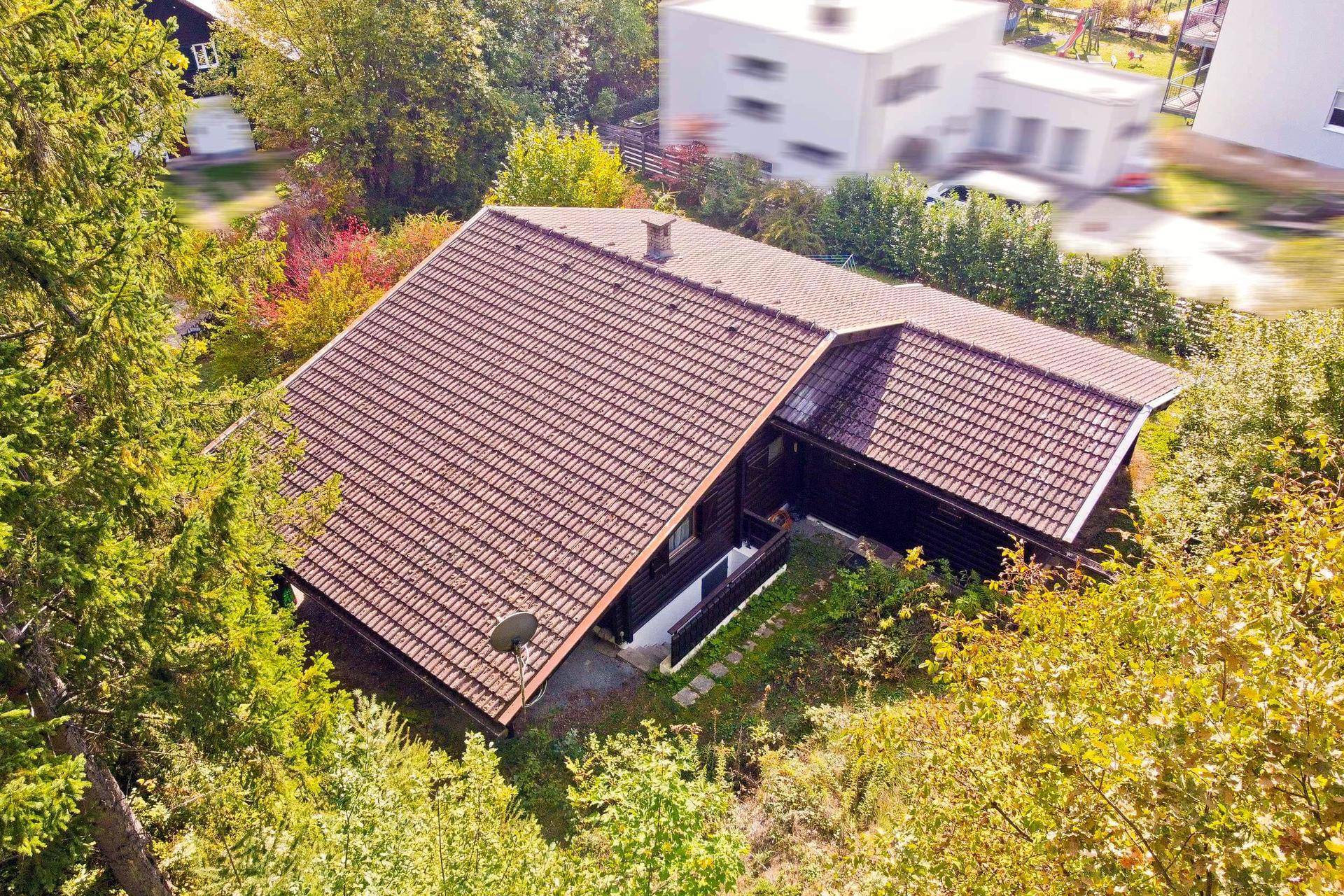 Rückansicht des Holzchalets mit großem Ziegeldach, eingebettet in die herbstliche Waldlandschaft.