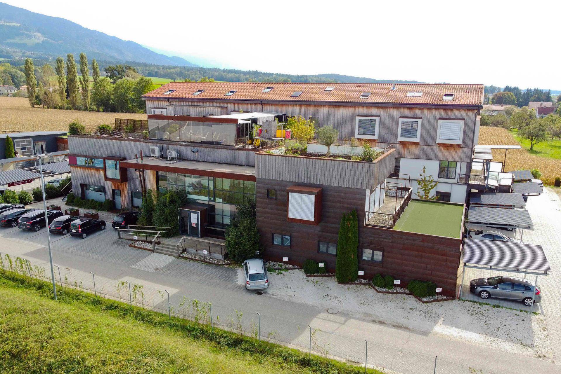 Moderner Gebäudekomplex mit Holzfassade, großen Fenstern und Carports in ländlicher Umgebung.