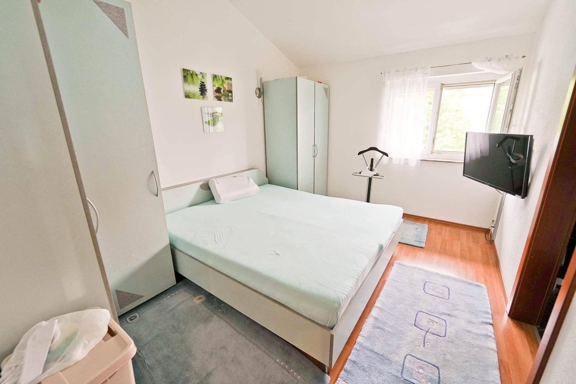 Helles Schlafzimmer mit Doppelbett, Kleiderschränken und einem Fenster, das Tageslicht hereinlässt.