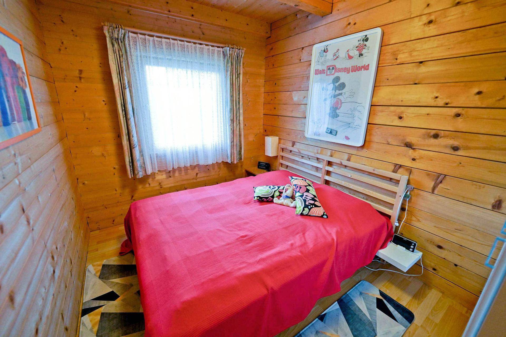 Helles Schlafzimmer mit Holzwänden, Doppelbett und einem Fenster für natürliche Belichtung.