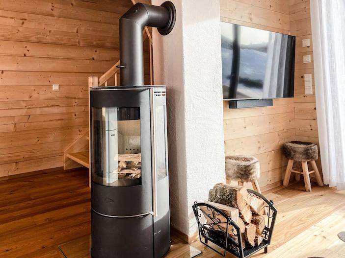 Moderner Kaminofen im Wohnzimmer mit Holzscheiten und Fernseher an der Wand.