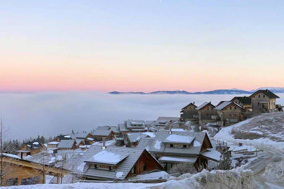 Winterliche Landschaft mit verschneiten Häusern und einer dichten Nebeldecke über dem Tal.