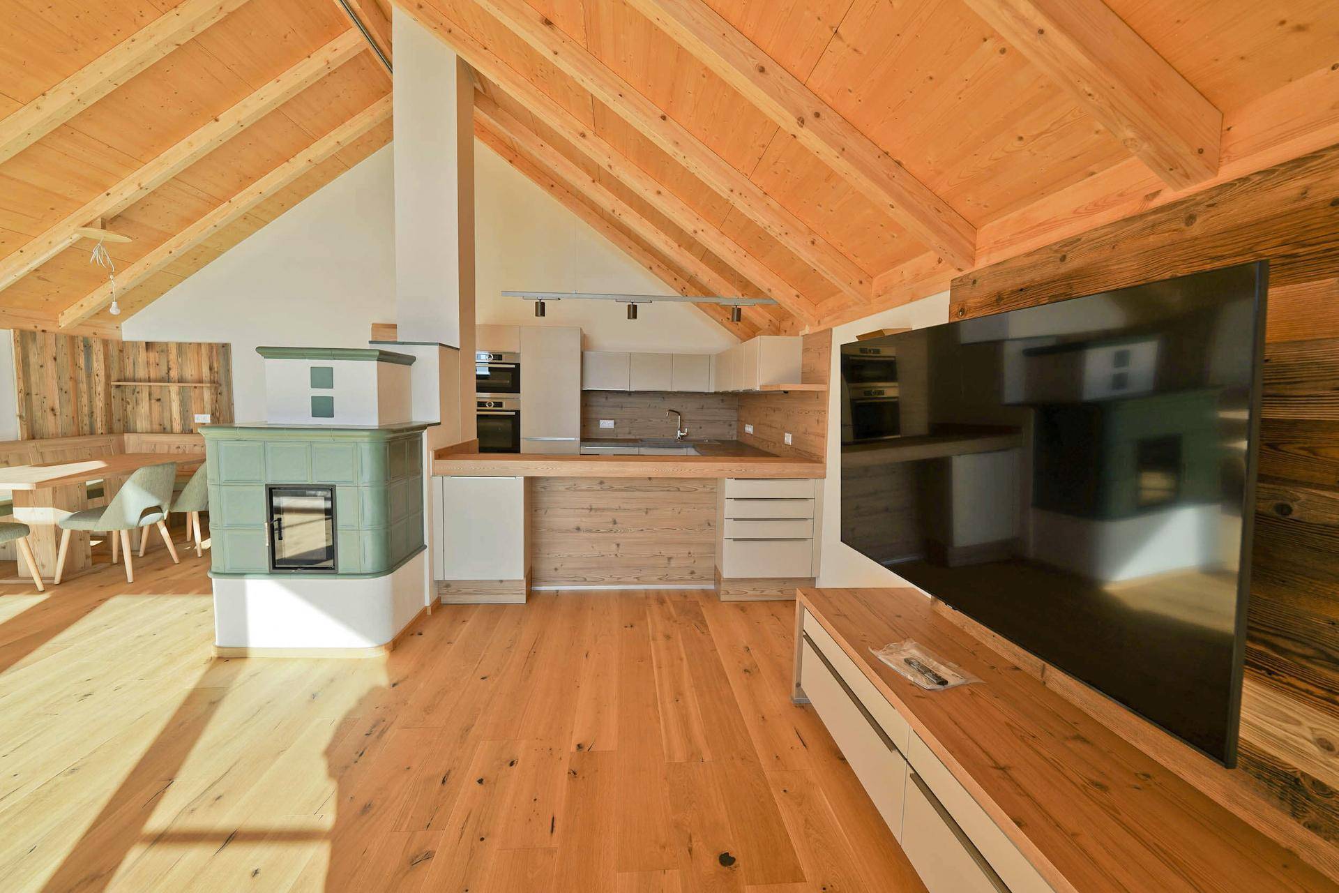 Offener Wohn-Essbereich mit Holzdachschrägen, Kachelofen und integrierter Küche in hellem Design.