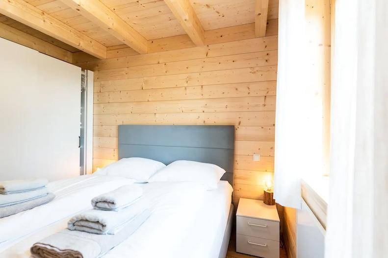 Helles Schlafzimmer mit Holzwänden, Doppelbett und Nachttischlampe.
