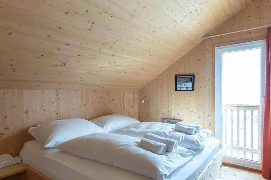 Gemütliches Schlafzimmer mit Doppelbett, Holzwänden und Zugang zu einem kleinen Balkon.