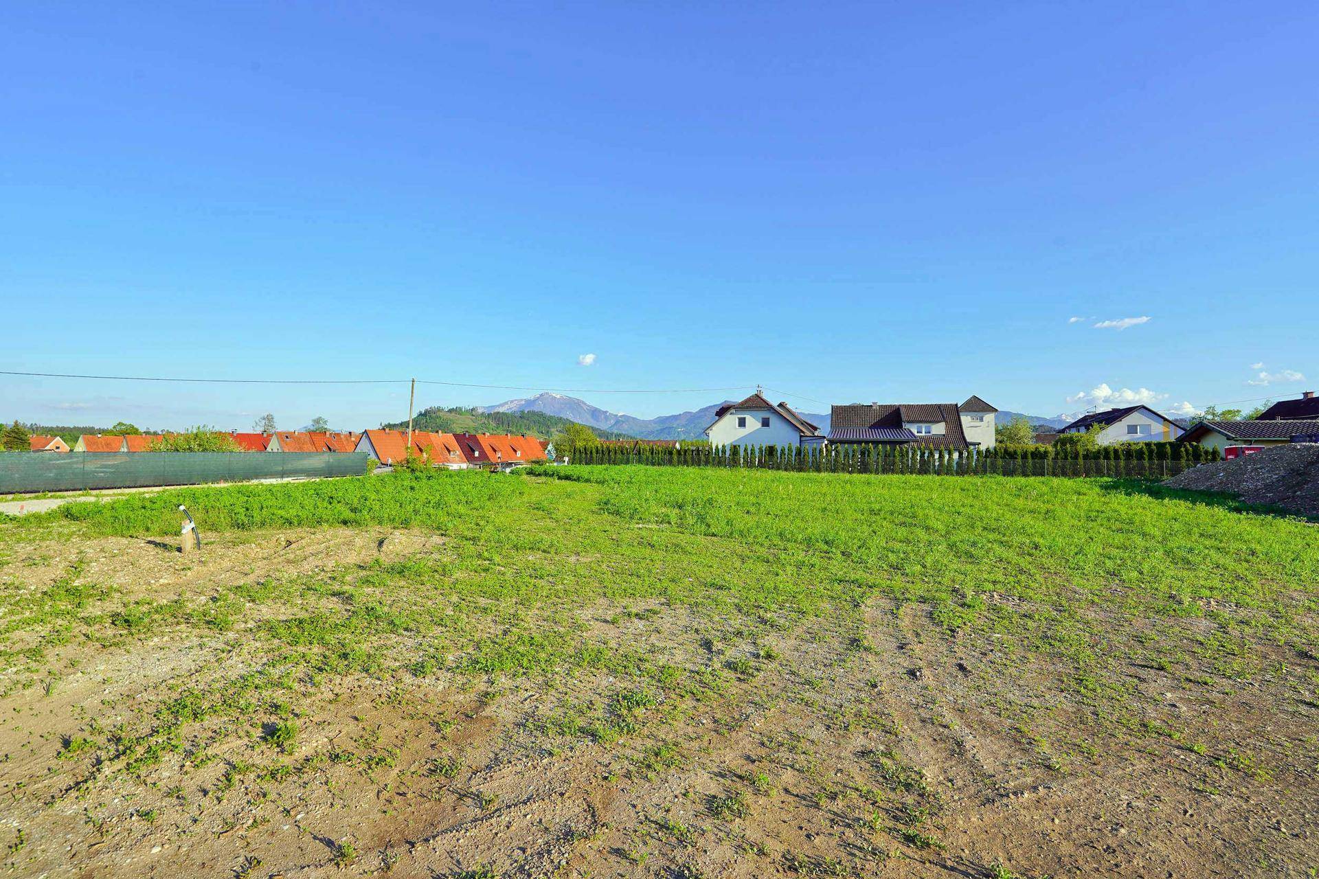 Offenes Baugrundstück mit Blick auf die umliegende Wohnbebauung und die Berglandschaft.