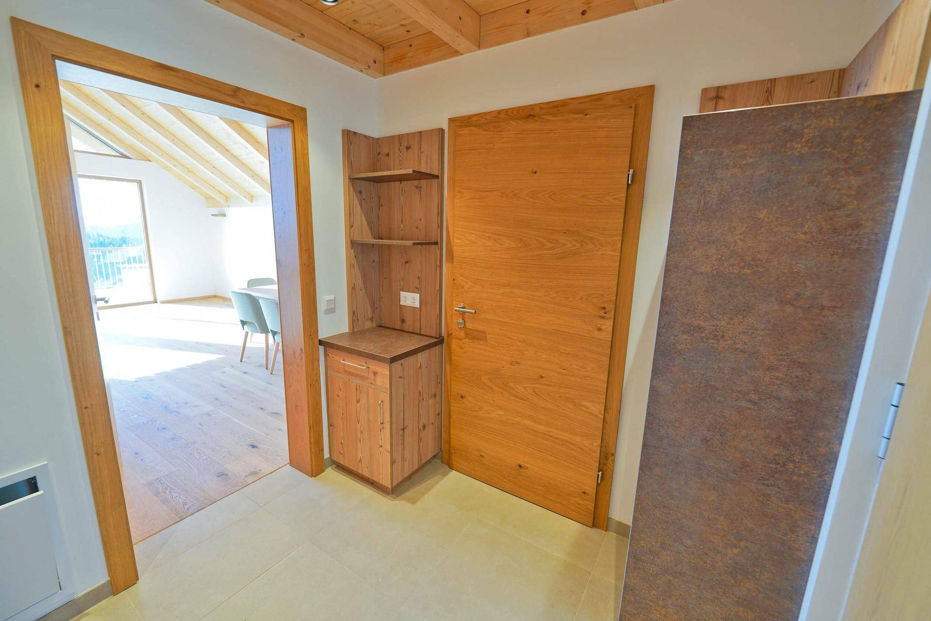 Heller Eingangsbereich mit Holztüren, Einbauschrank und Fliesenboden unter einer Holzdecke.
