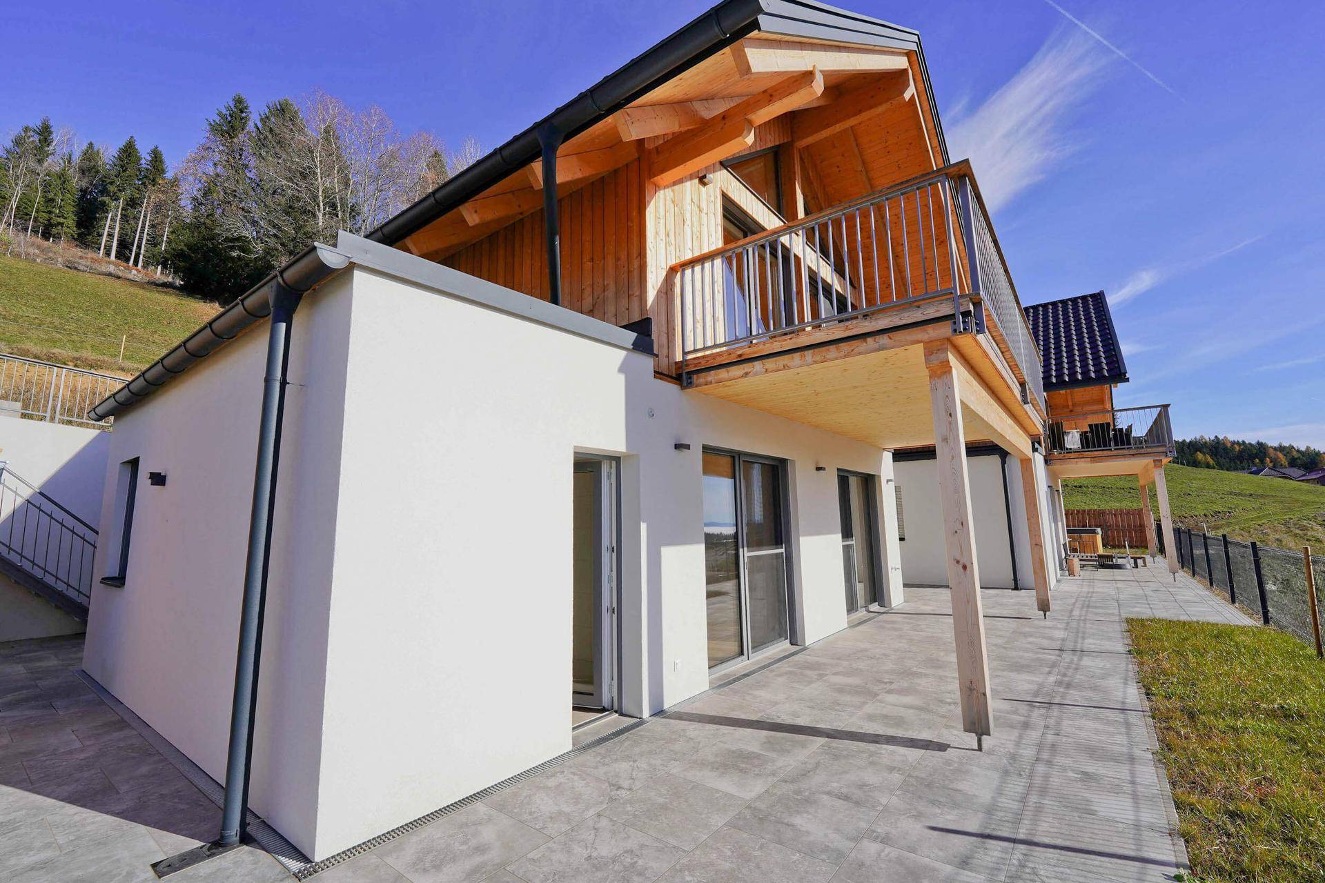 Seitliche Ansicht eines Holzhauses mit großer, überdachter Terrasse und großen Fenstern zur Natur.