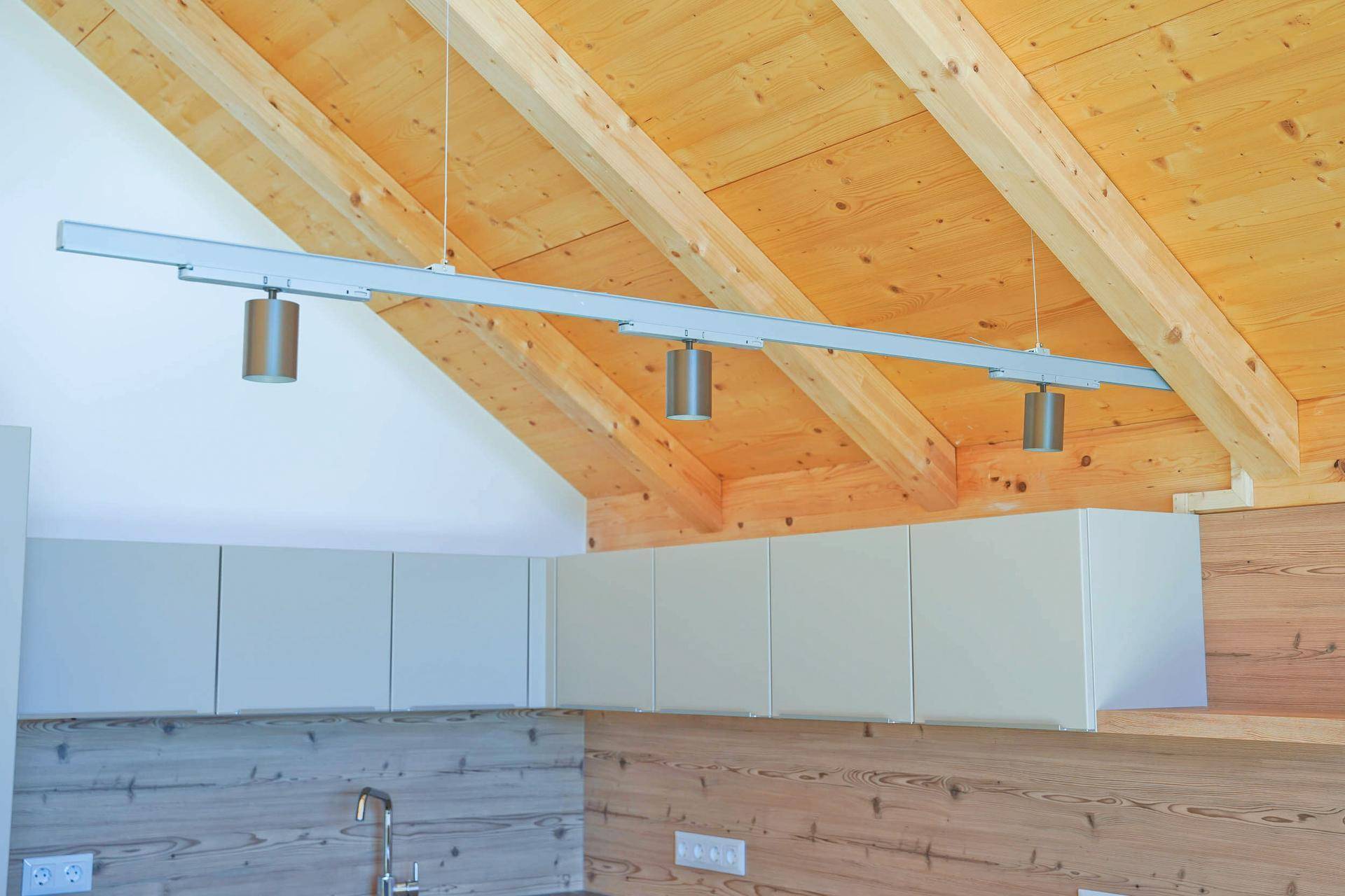 Holzdachschräge mit sichtbaren Balken und moderner Hängeleuchte über der Küche.