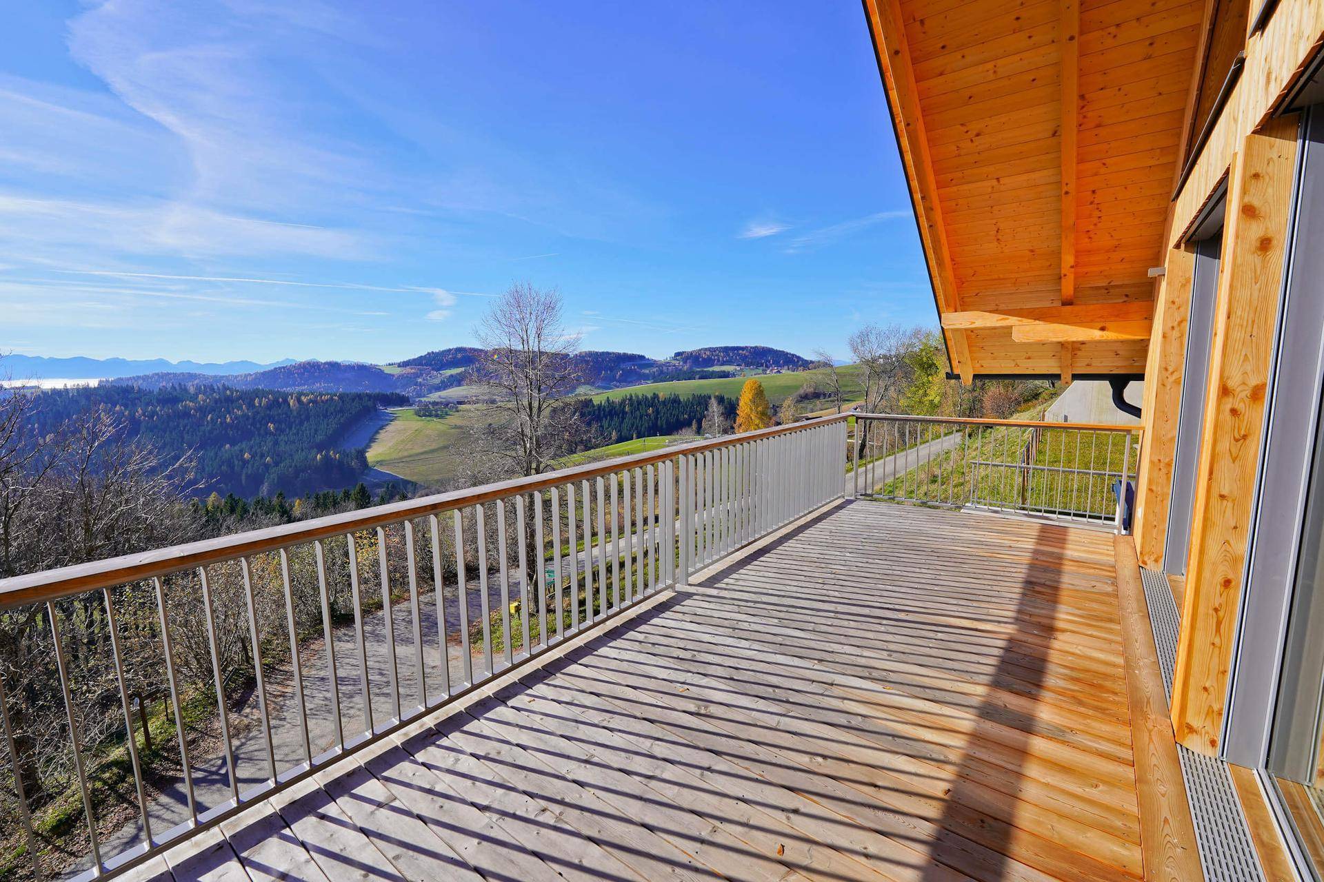 Geräumiger Holzbalkon mit weitem Blick über die grüne Hügellandschaft unter blauem Himmel.