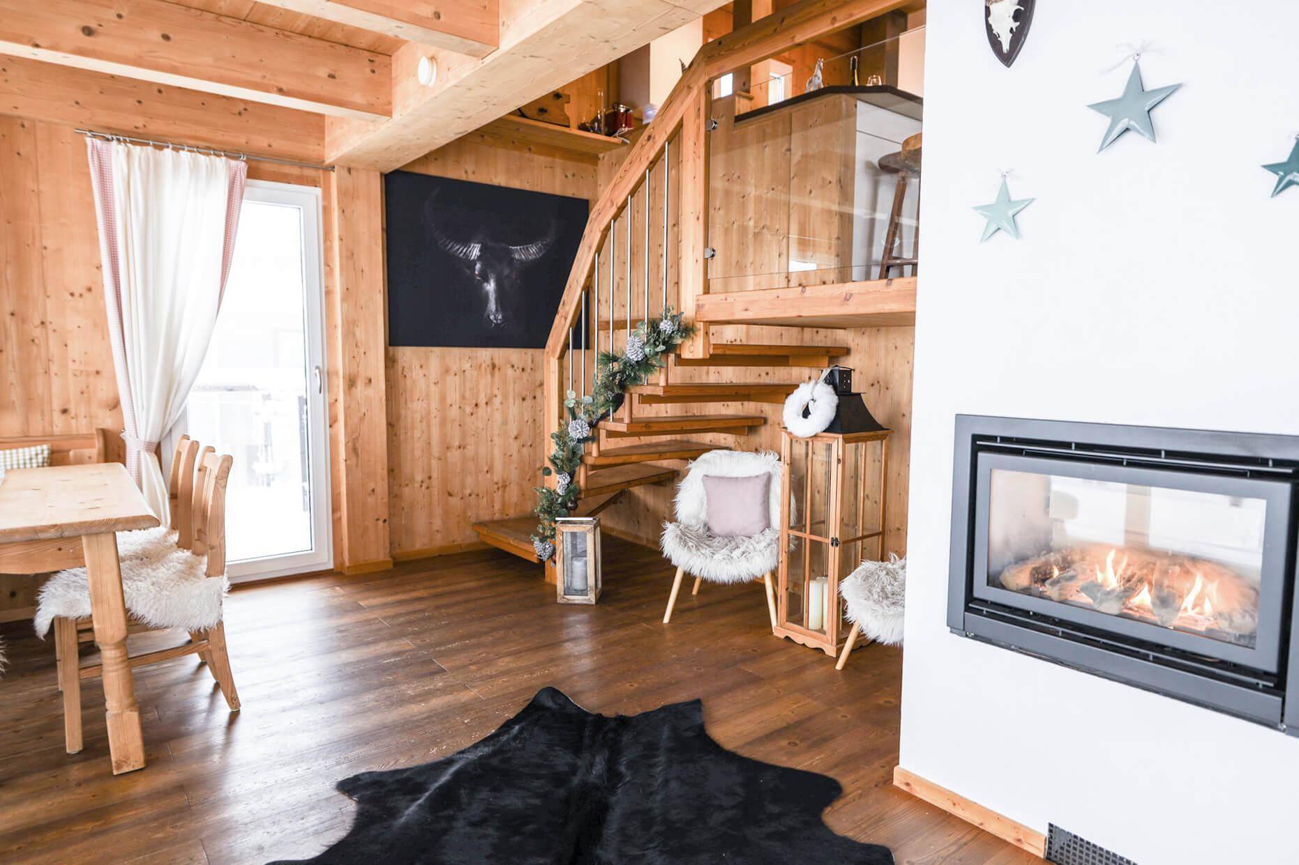 Offener Wohn- und Essbereich mit Kamin, Holztreppe und rustikal-modernem Dekor.