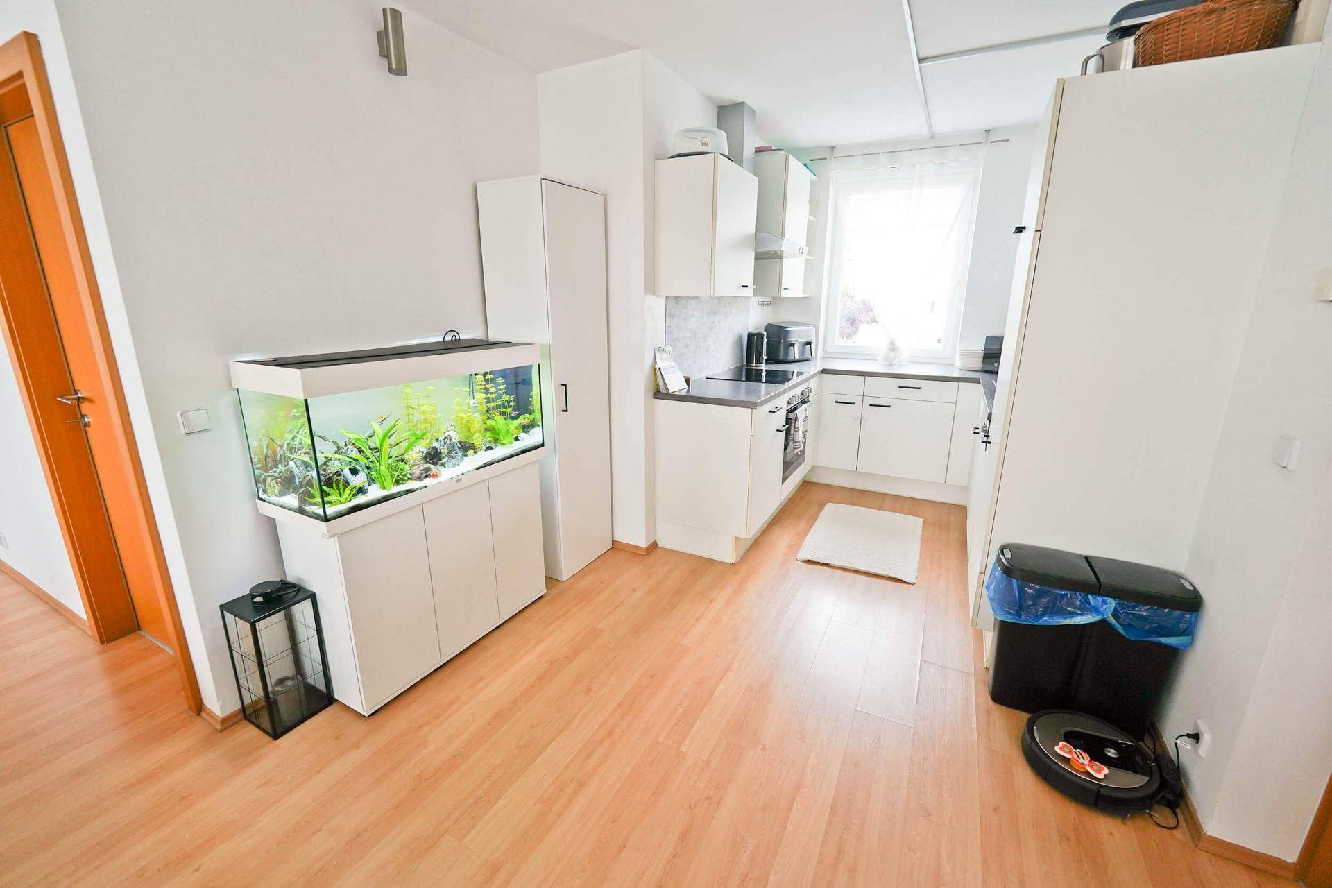 Kleine, helle Küche mit weißen Schränken, Holzboden und integriertem Aquarium.