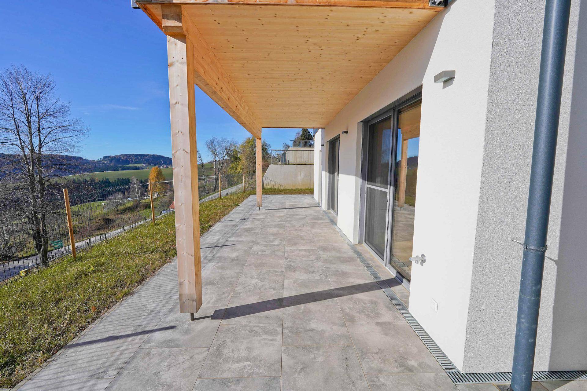 Überdachte Terrasse mit Holzbalken und weitem Blick über die grüne Landschaft.