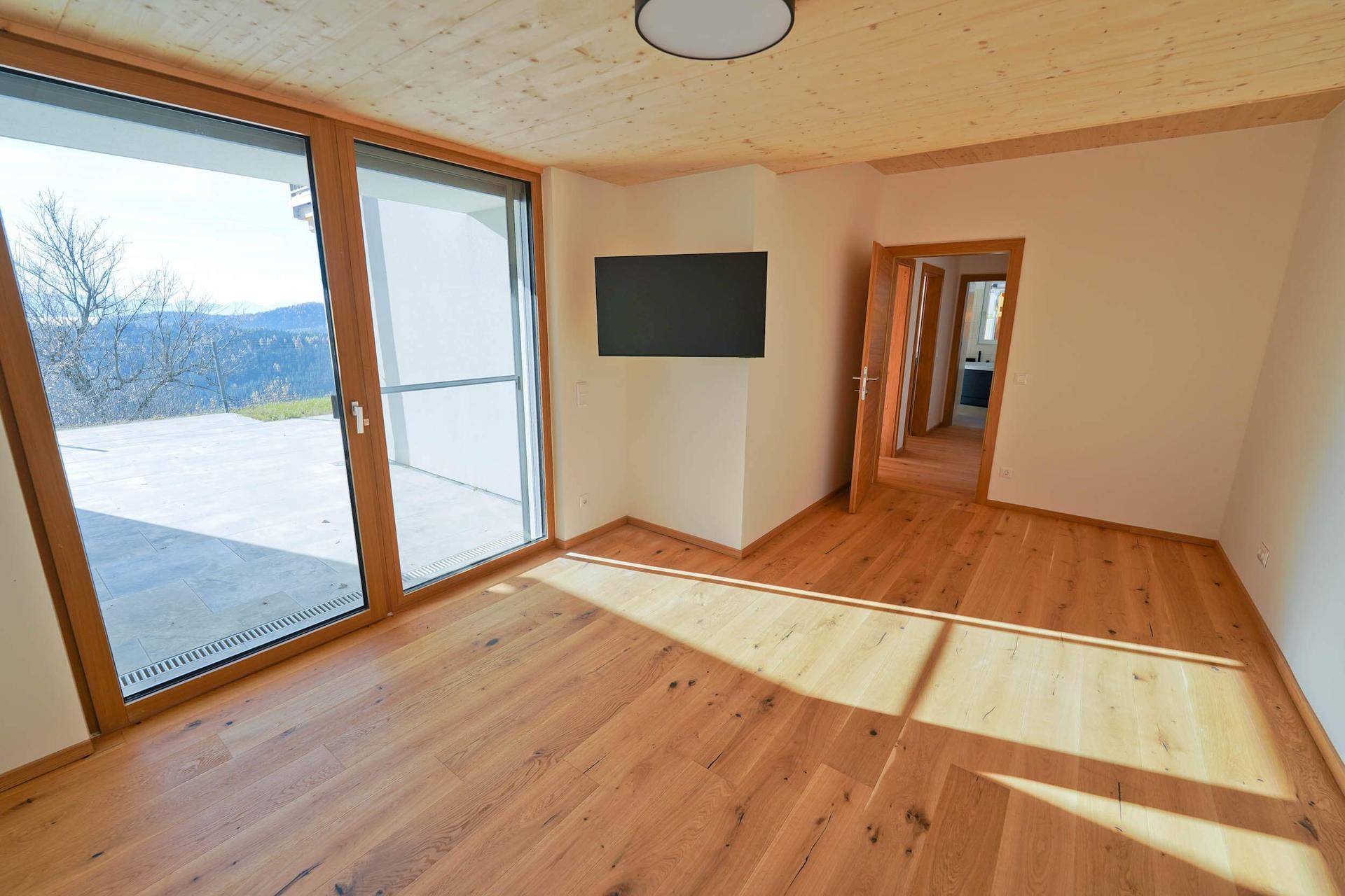 Geräumiges Zimmer mit Holzboden, Terrassenzugang und Blick in die weite Landschaft.