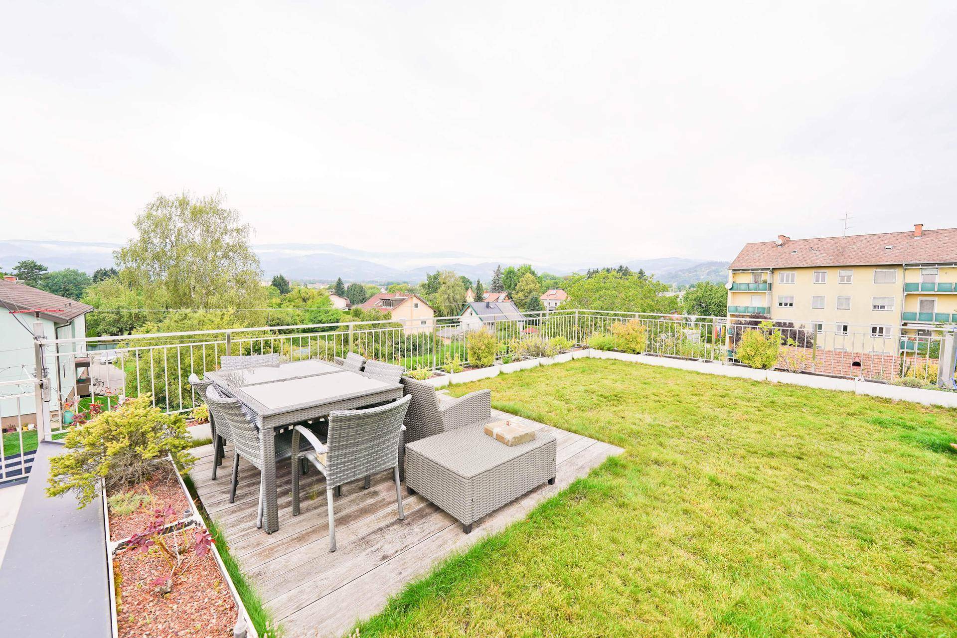 Große Dachterrasse mit Rasenfläche, Gartenmöbeln und Panoramablick über die Umgebung.