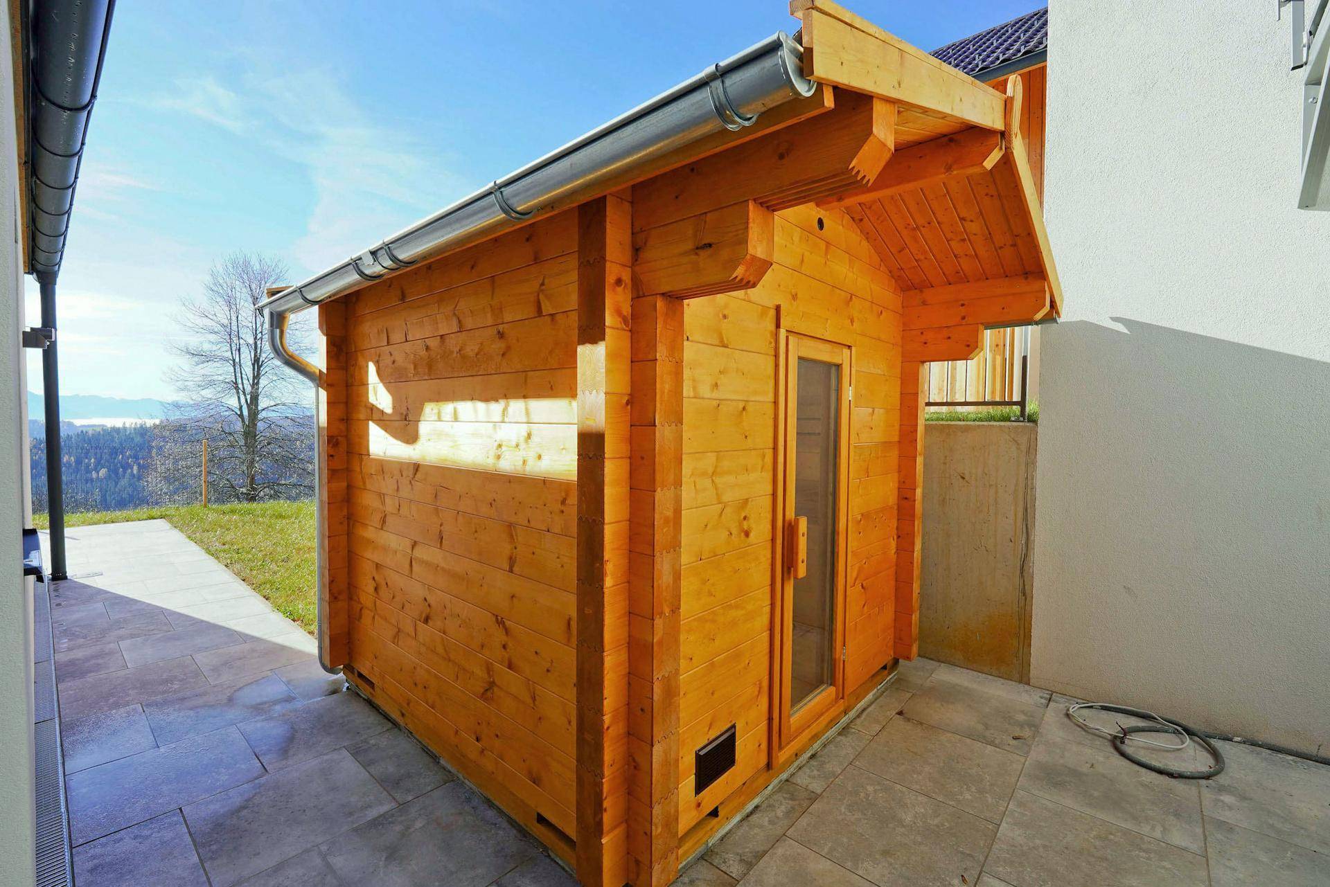 Kleines Holzgartenhaus neben dem Hauptgebäude auf einer gepflasterten Fläche.