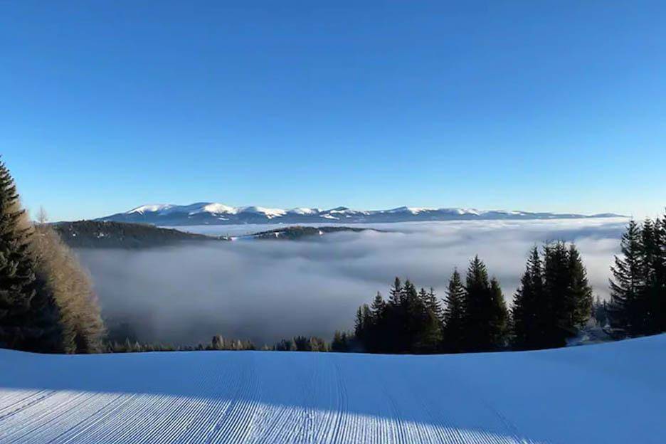Weitläufige Winterlandschaft mit verschneiten Bergen und einem Nebelmeer im Tal.