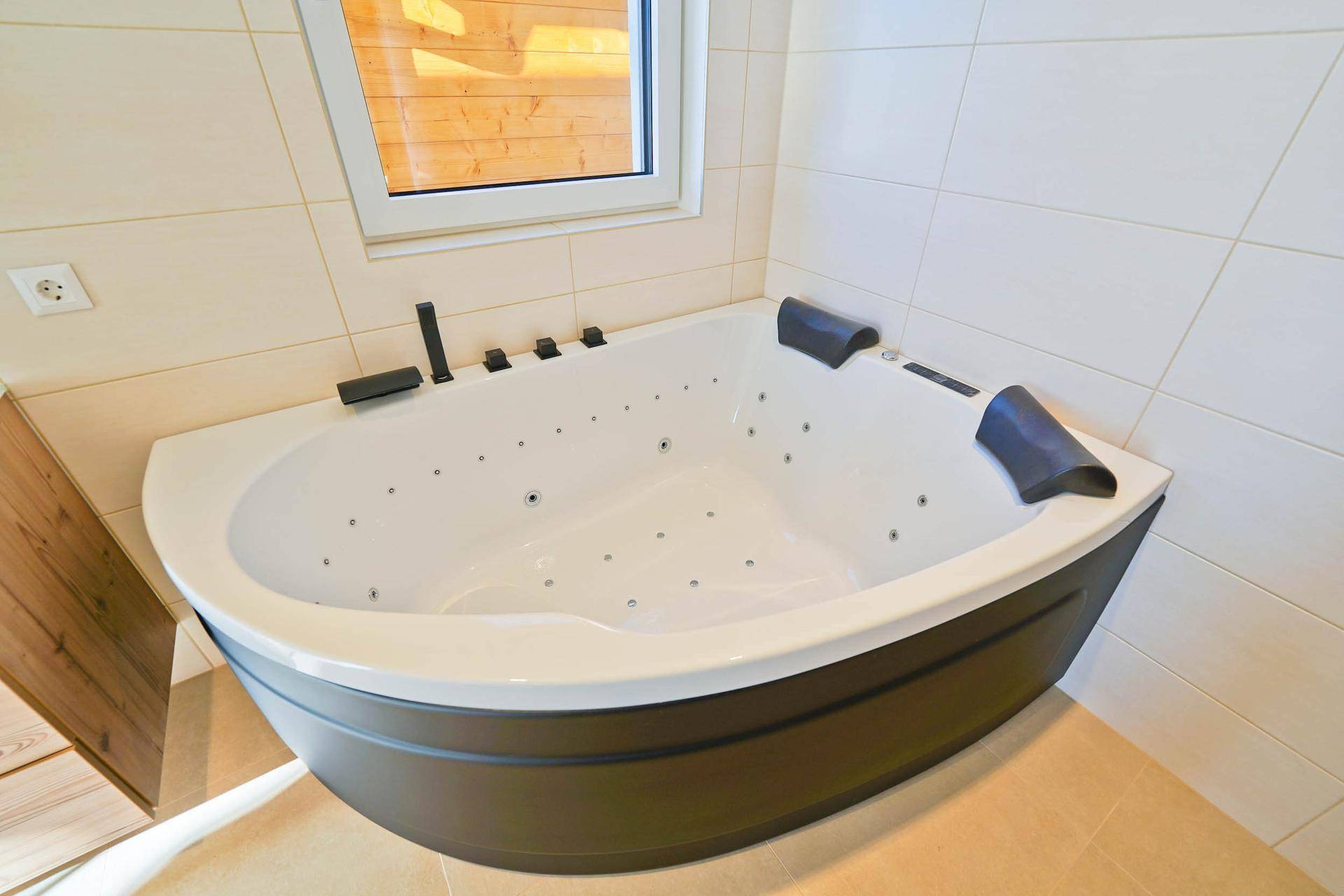 Moderne Eckbadewanne mit Whirlpool-Funktion und Fenster in einem hellen Badezimmer.