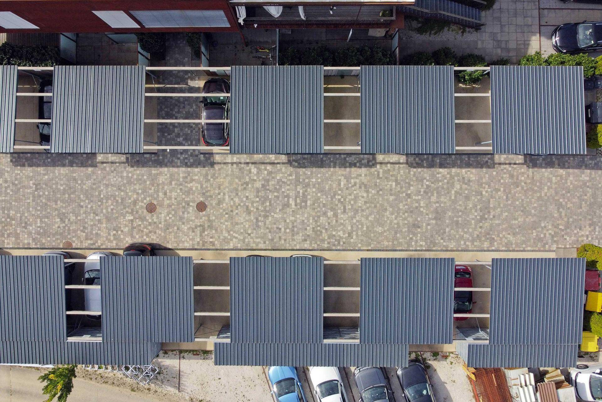 Reihen von Carports und Parkplätzen auf einem gepflasterten Bereich neben dem Wohnkomplex.