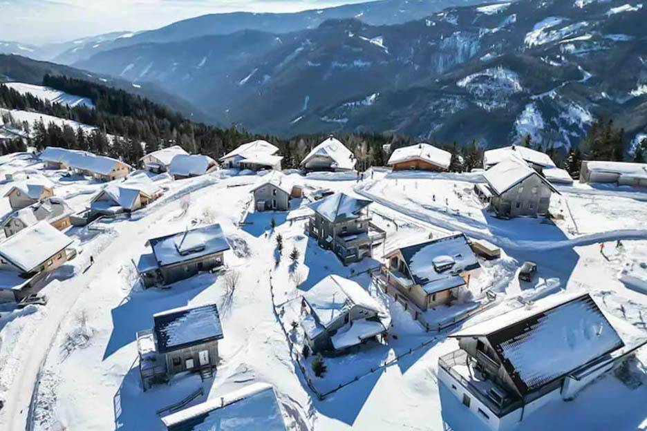 Luftaufnahme eines verschneiten Bergdorfes mit vielen Holzhäusern in alpiner Umgebung.