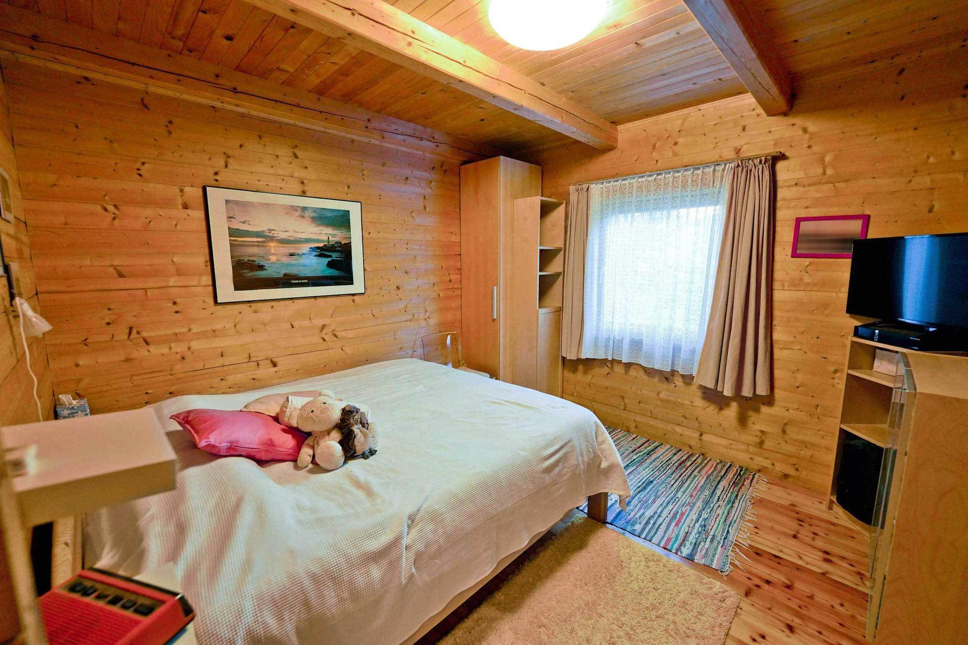 Gemütliches Schlafzimmer mit Holzwänden, Doppelbett und einem Fenster mit Blick ins Grüne.