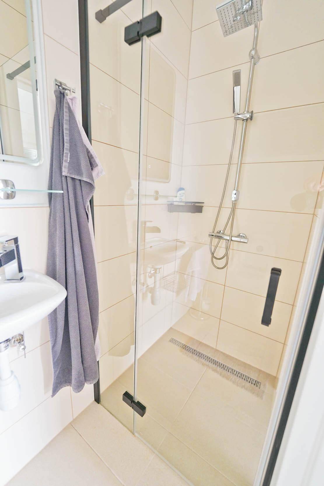 Modernes Badezimmer mit begehbarer Dusche, hellen Fliesen und minimalistischem Design.