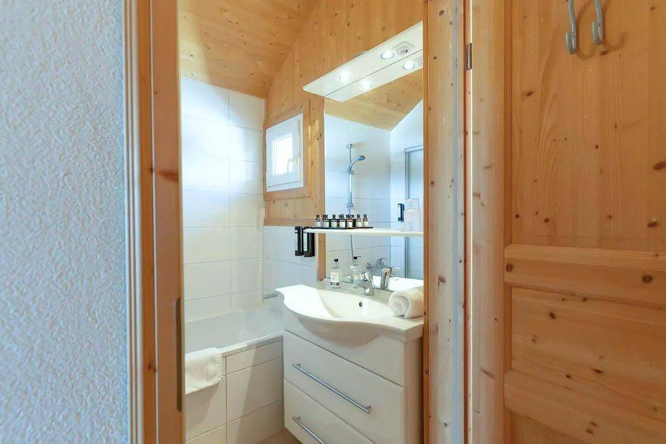 Helles Badezimmer mit Badewanne, Duschfunktion und Holzverkleidung an den Wänden.