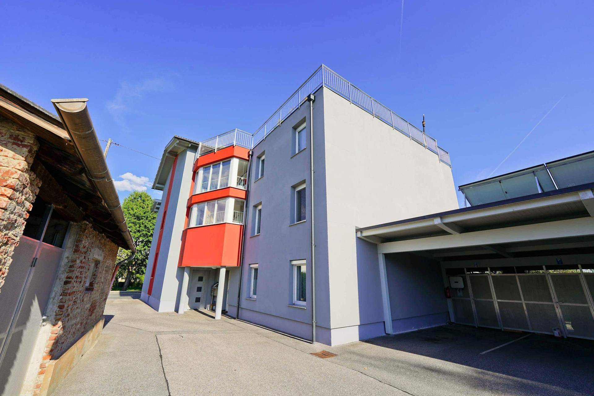Seitenansicht des modernen Gebäudes mit integriertem Carport und rotem Fassadenakzent.